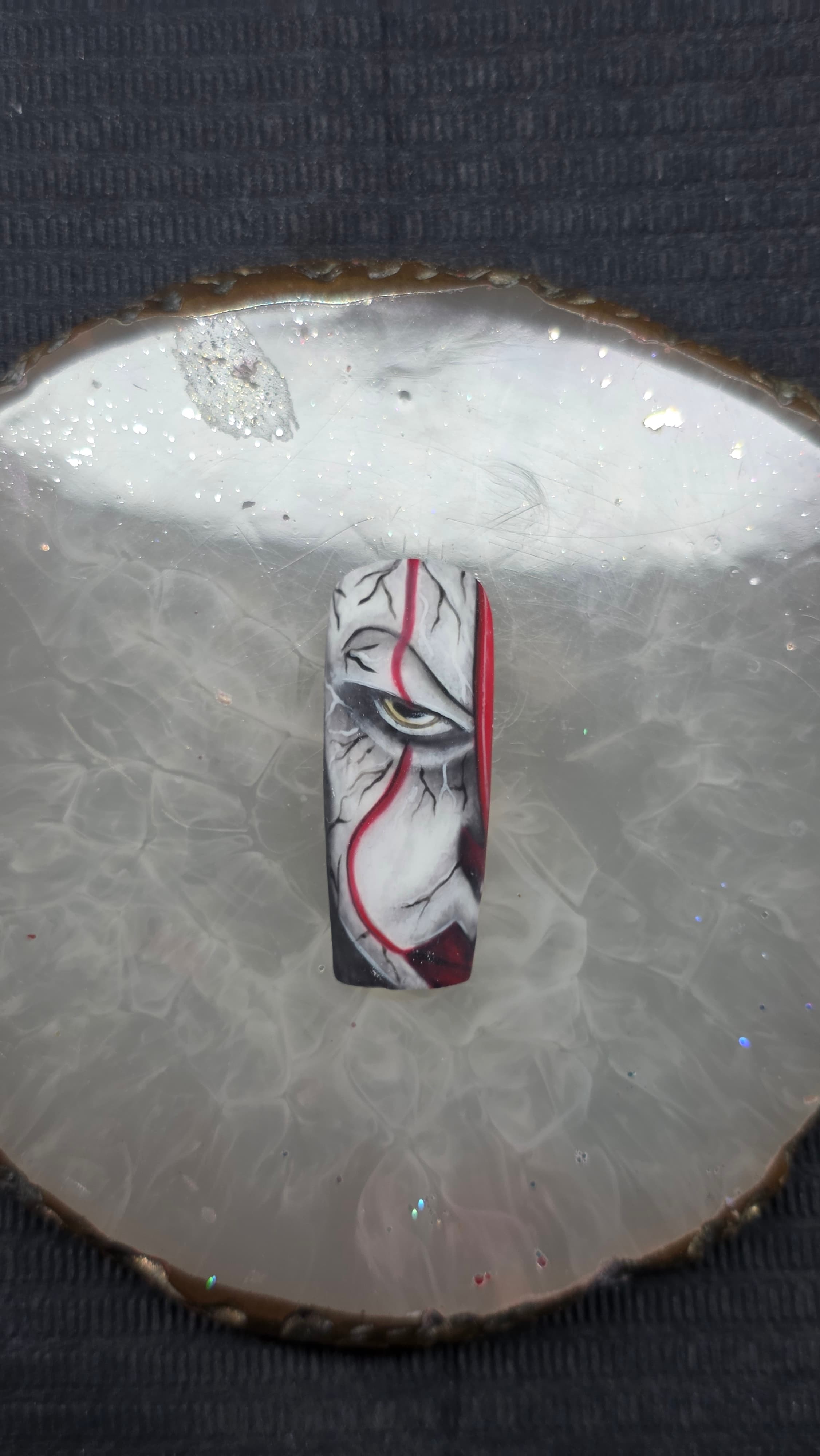 Faux ongle avec un œil de clown sinistre, des fissures et des lignes rouges vives.