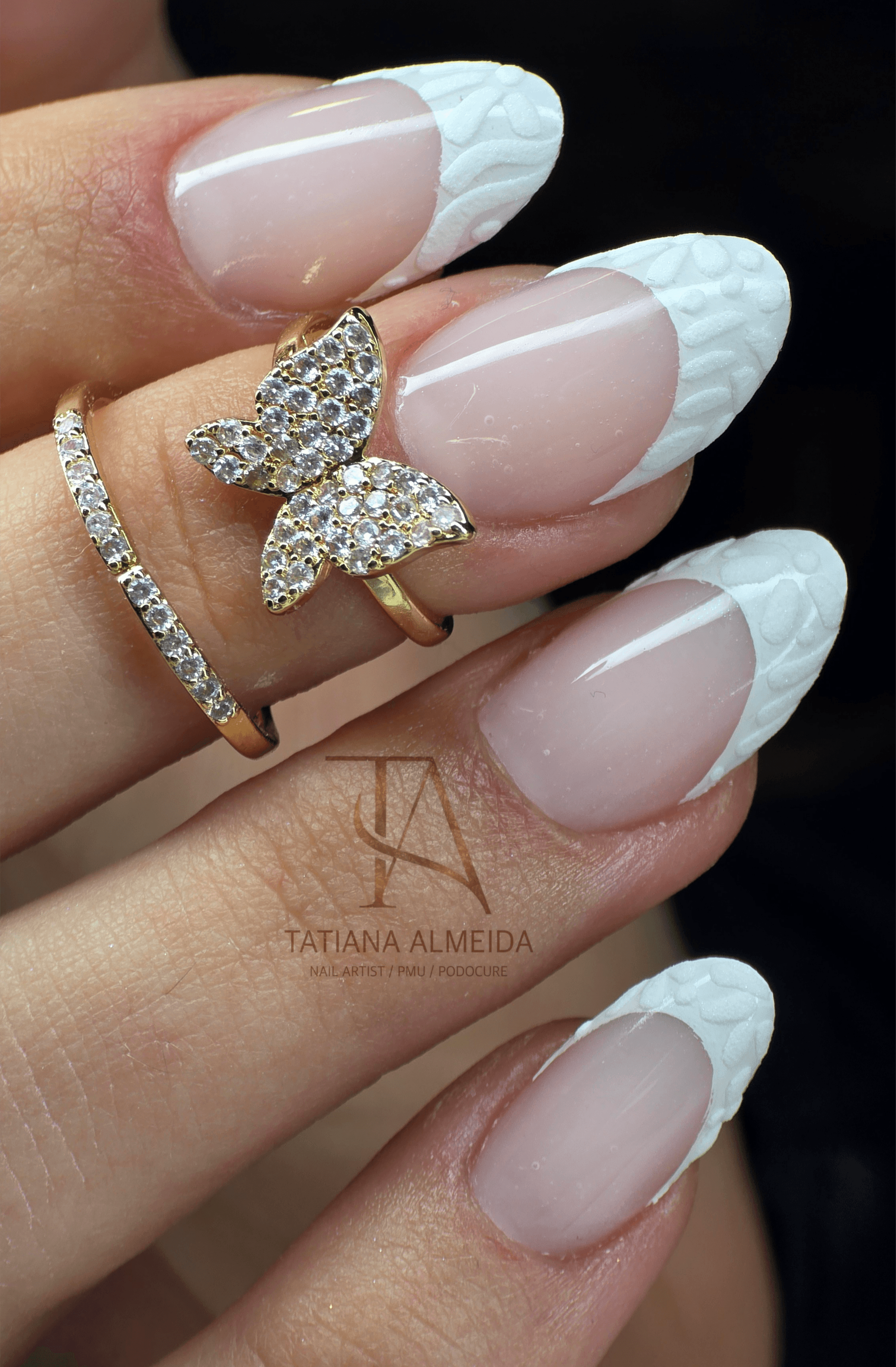 Manucure française élégante avec pointes blanches texturées et bagues dorées ornées de cristaux étincelants.