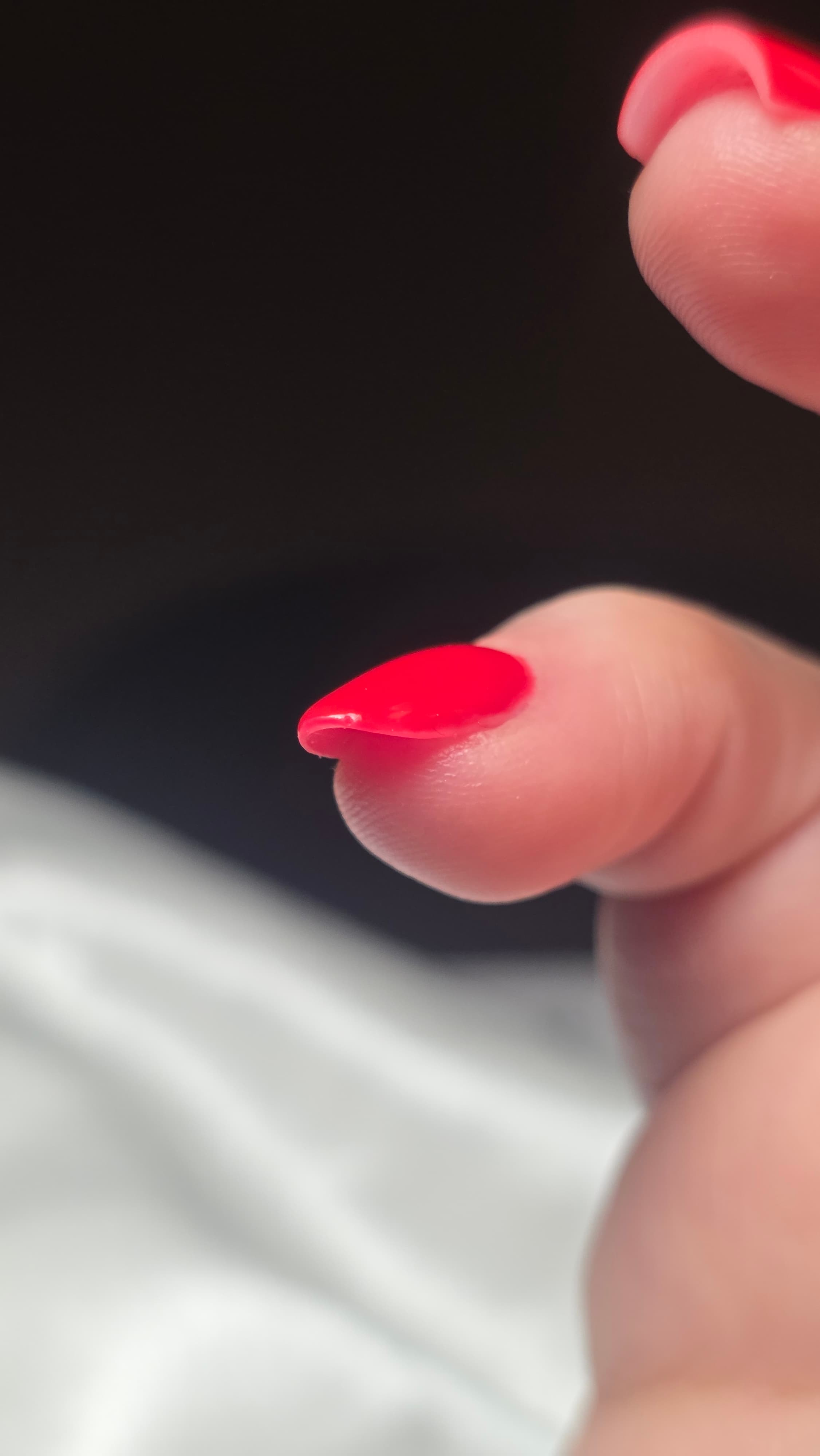 Gros plan d'un doigt avec un ongle pointu verni en rouge vif sur fond sombre.