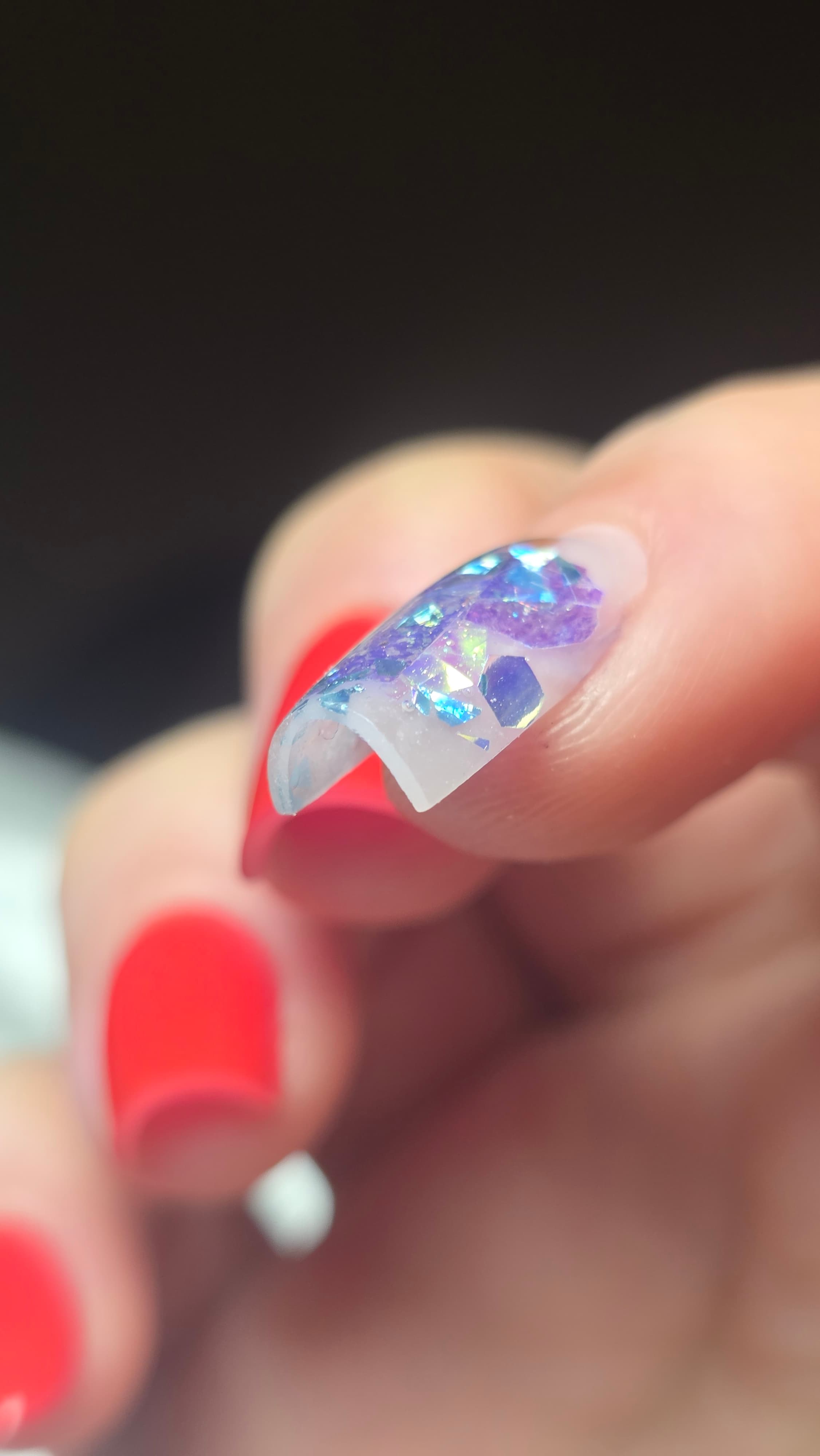 Gros plan d'un ongle en gel pailleté violet et bleu, présentant une cassure nette.