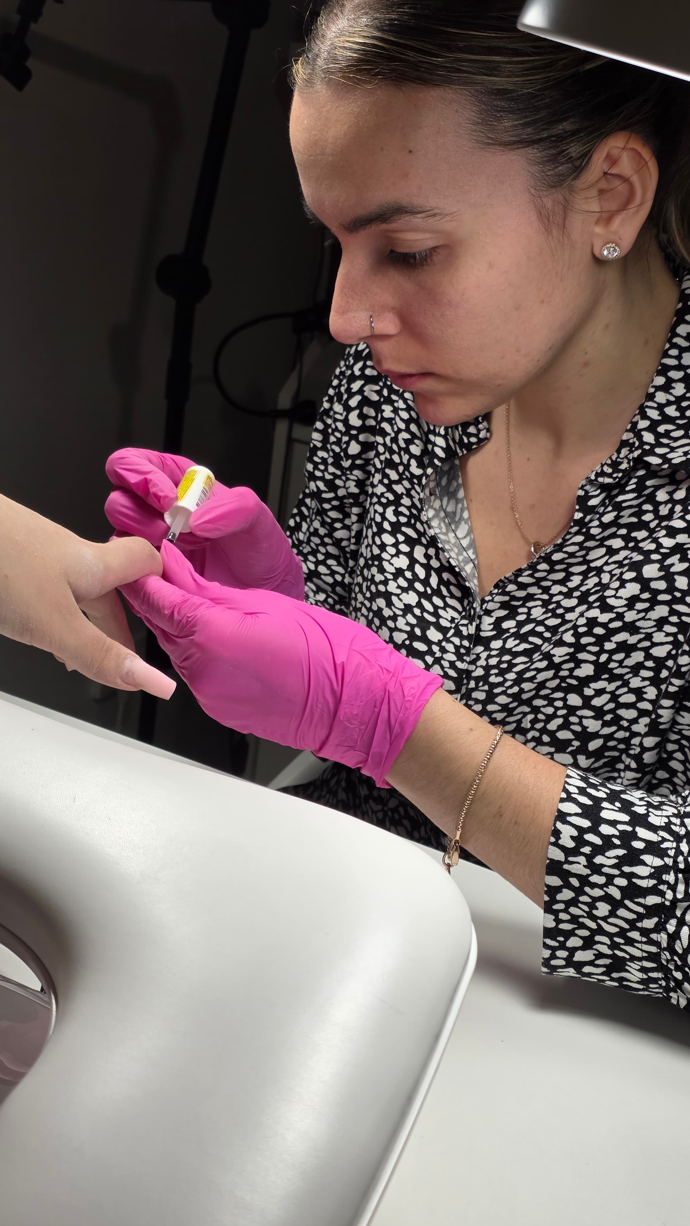 Une manucure portant des gants roses applique du vernis sur l'ongle long d'une cliente.