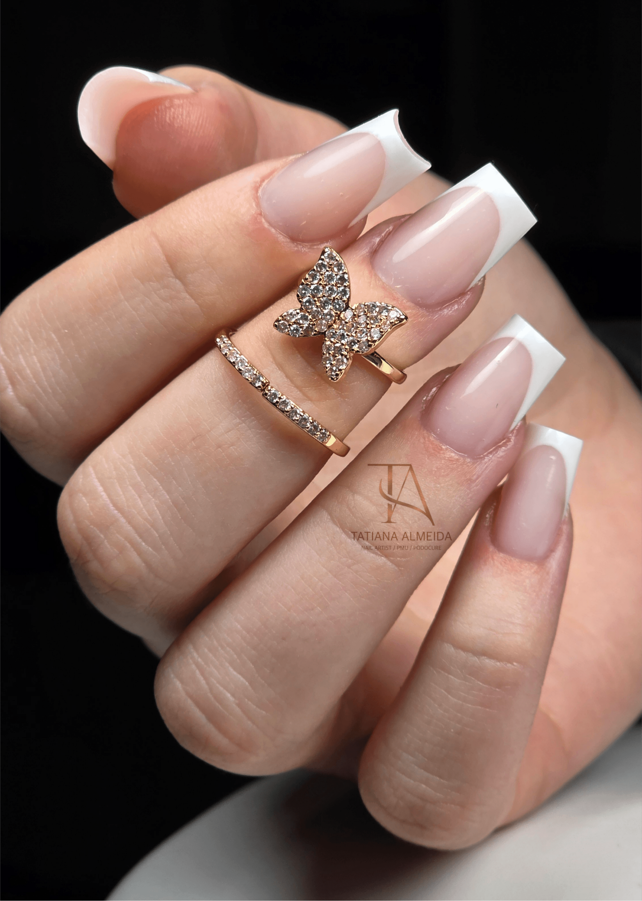 Manucure française sur ongles longs carrés avec bague papillon dorée et cristaux étincelants.