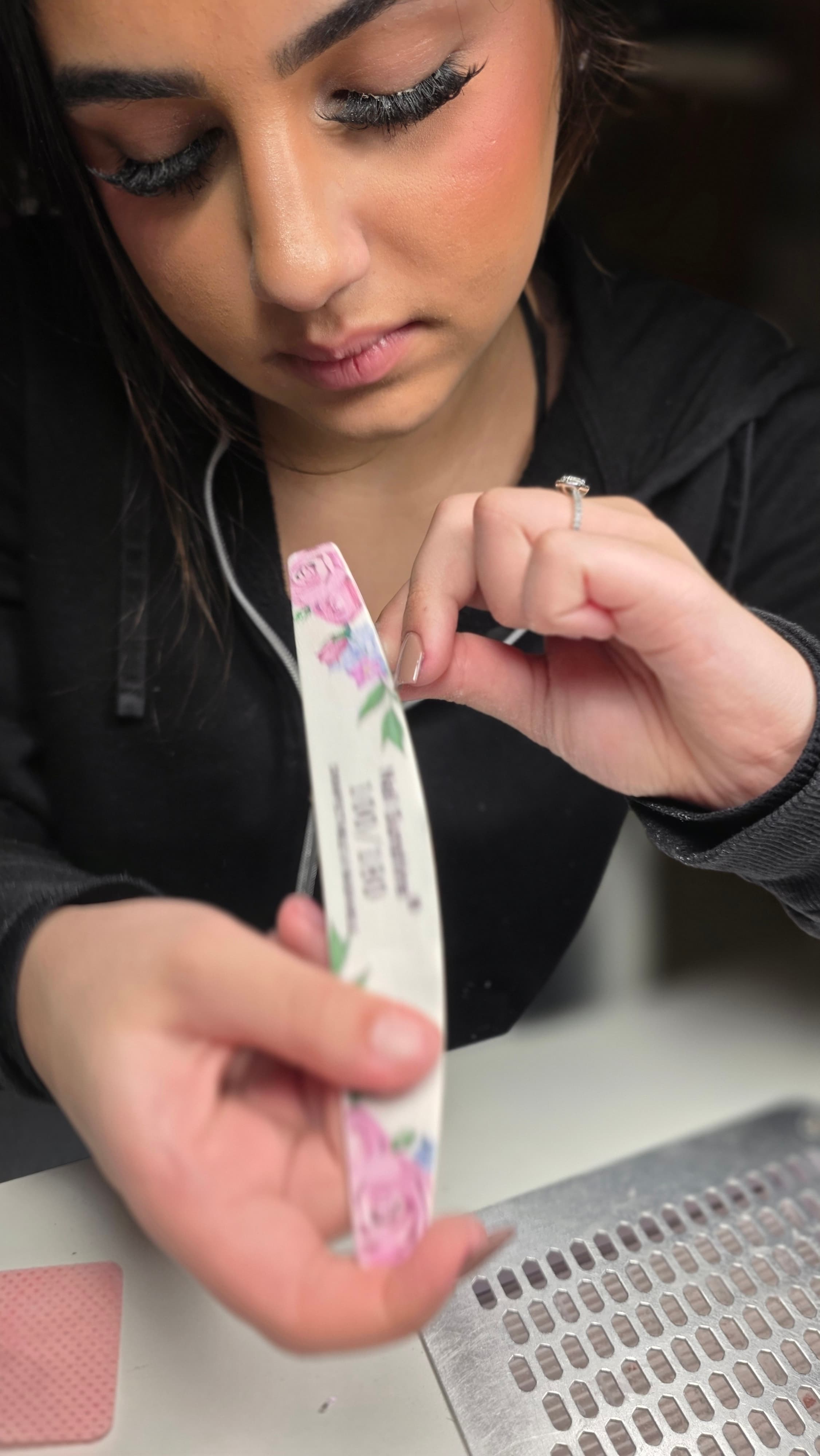 Une femme aux longs cils utilise une lime à ongles fleurie pour sa manucure.