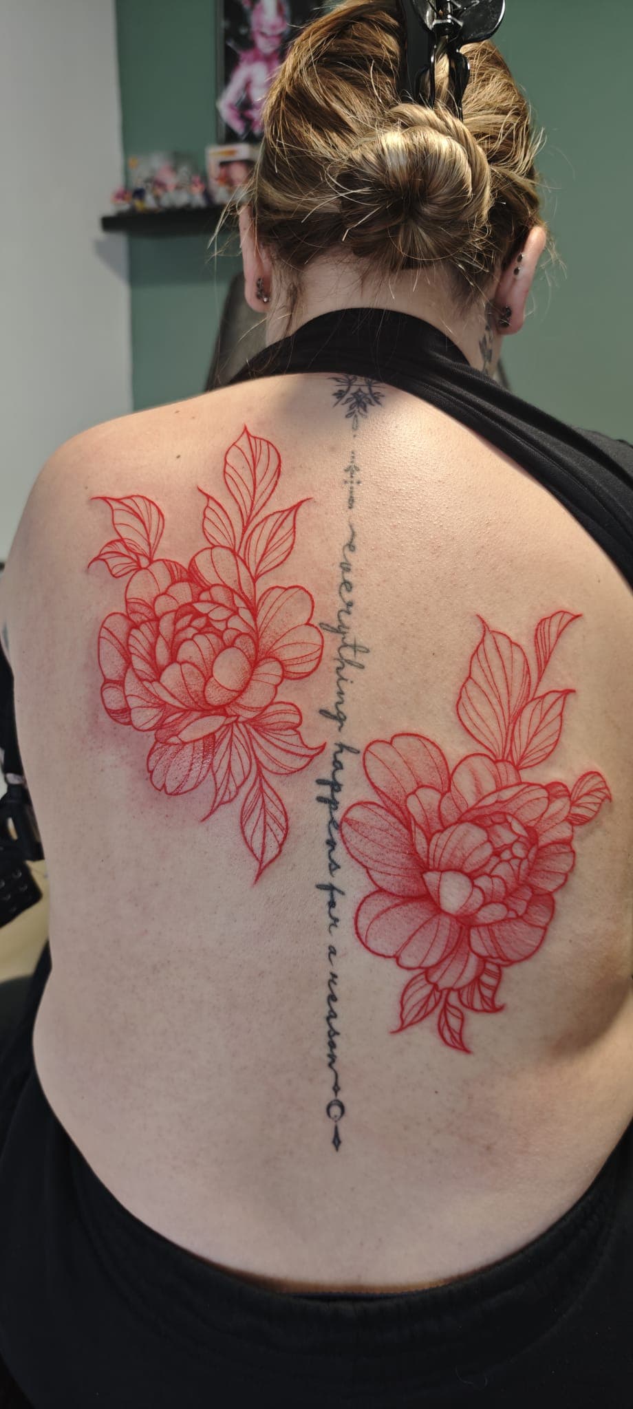 Tatouages de fleurs rouges sur les omoplates et citation verticale le long de la colonne.