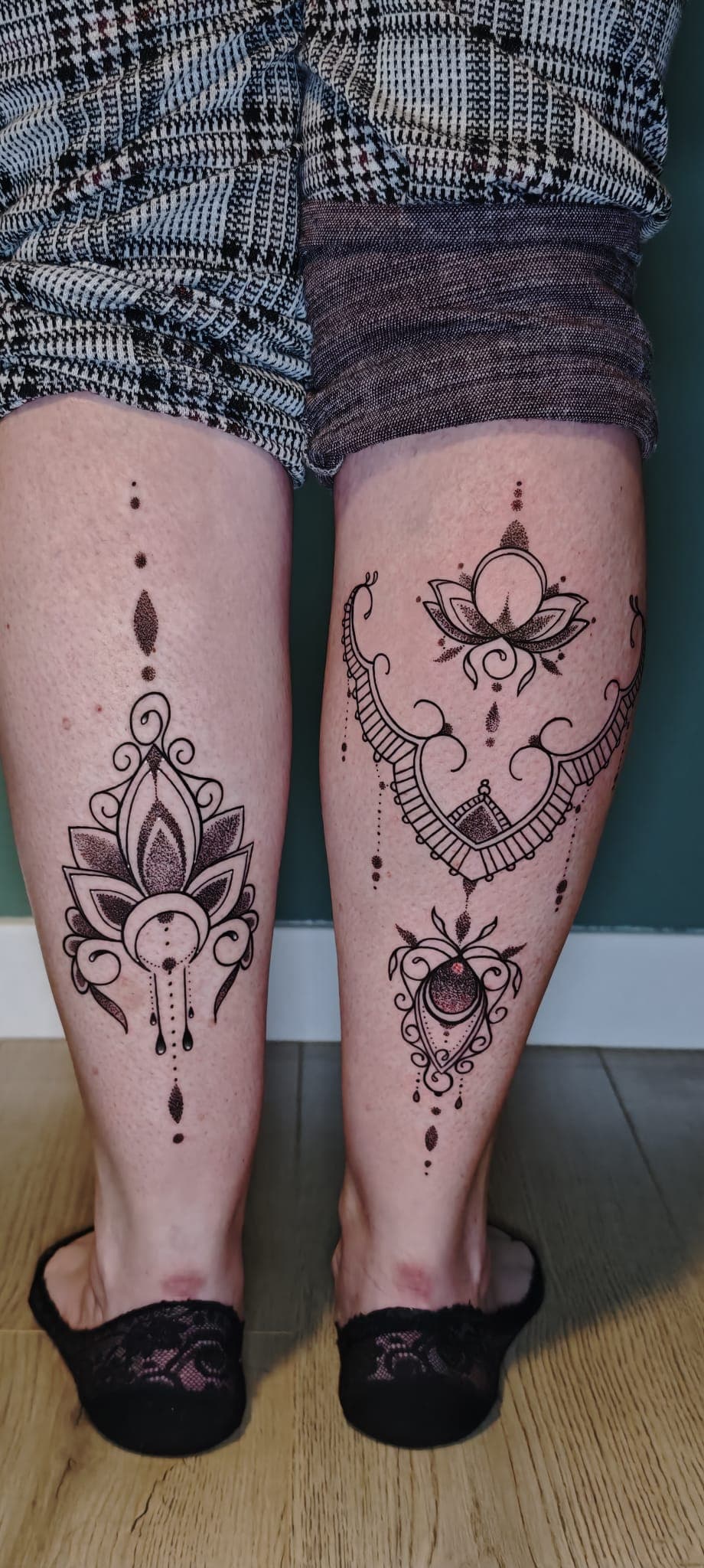 Tatouages noirs détaillés de fleurs de lotus et mandalas sur l'arrière des deux mollets.