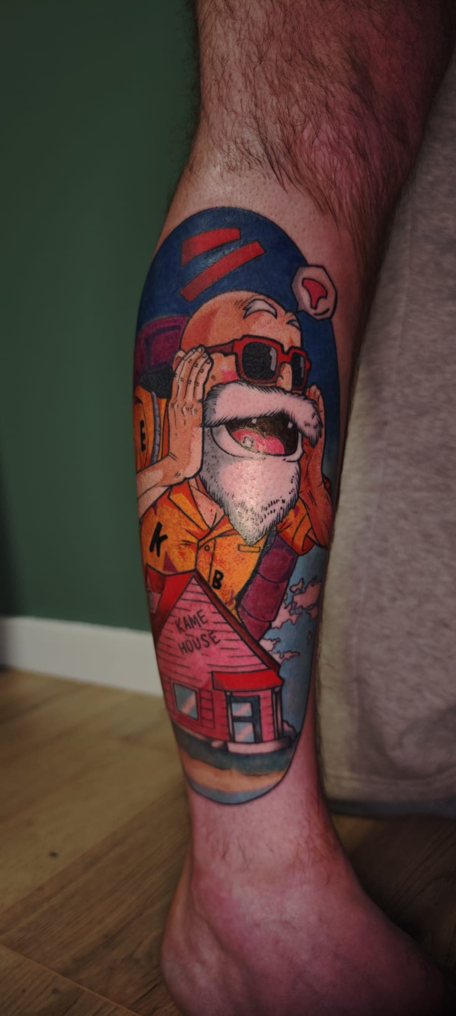 Tatouage coloré de Tortue Géniale criant, avec la Kame House en bas, sur un mollet.