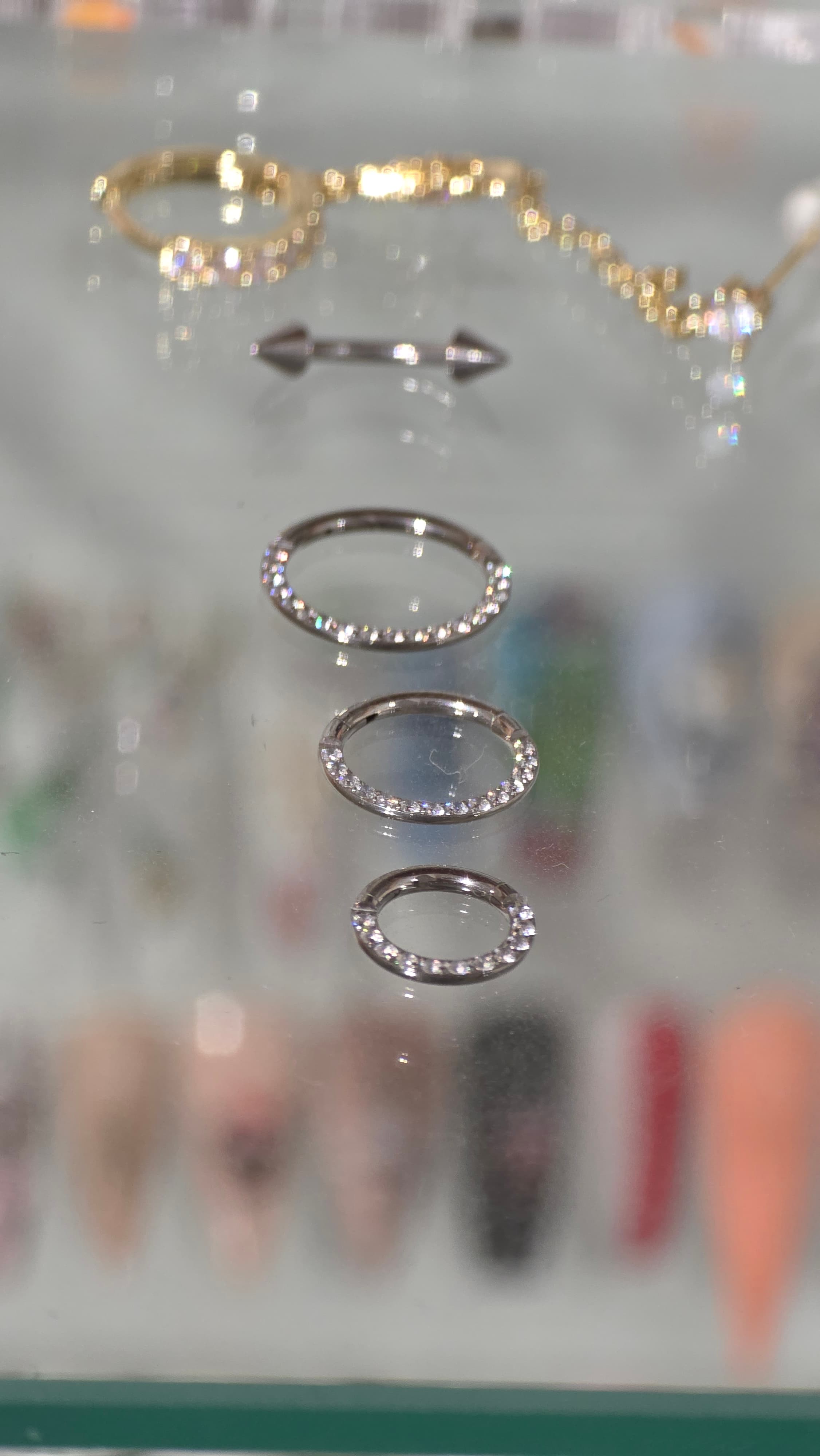 Trois anneaux de piercing argentés sertis de cristaux brillants alignés sur une surface vitrée.
