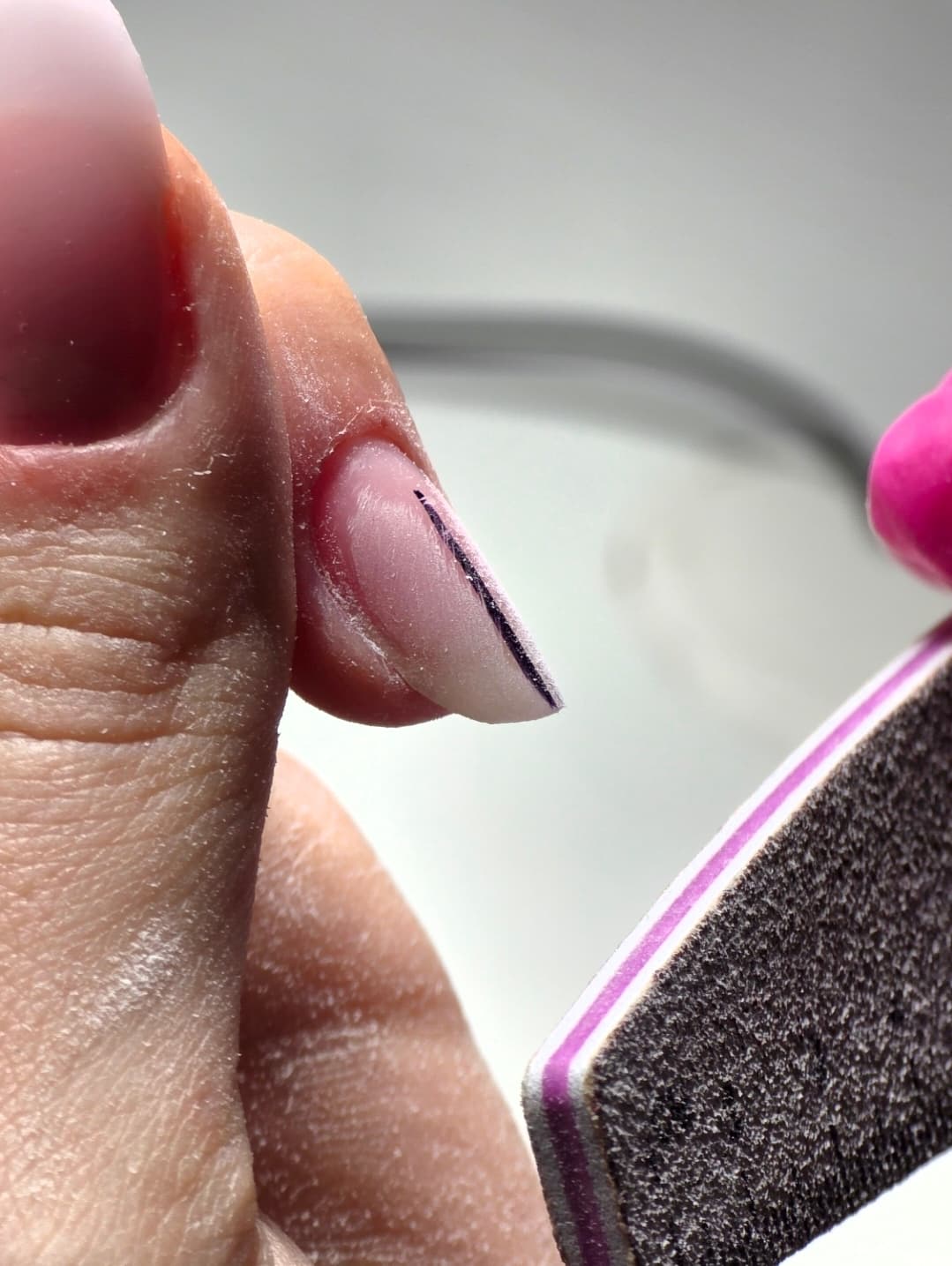 Une lime à ongles façonne un long ongle rose en amande avec un trait noir.