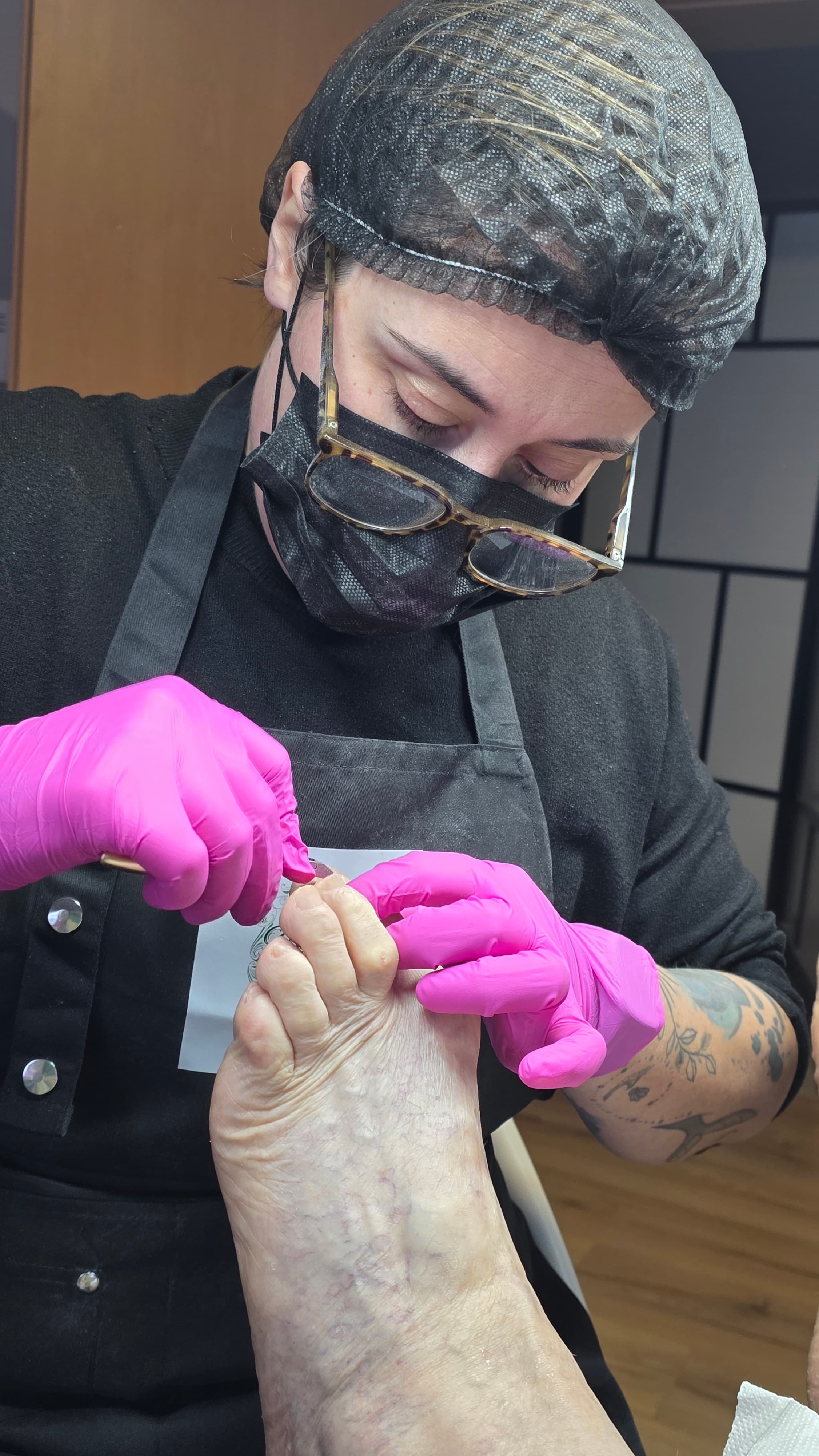 Une esthéticienne en gants roses et masque noir effectue un soin de pédicurie professionnel.