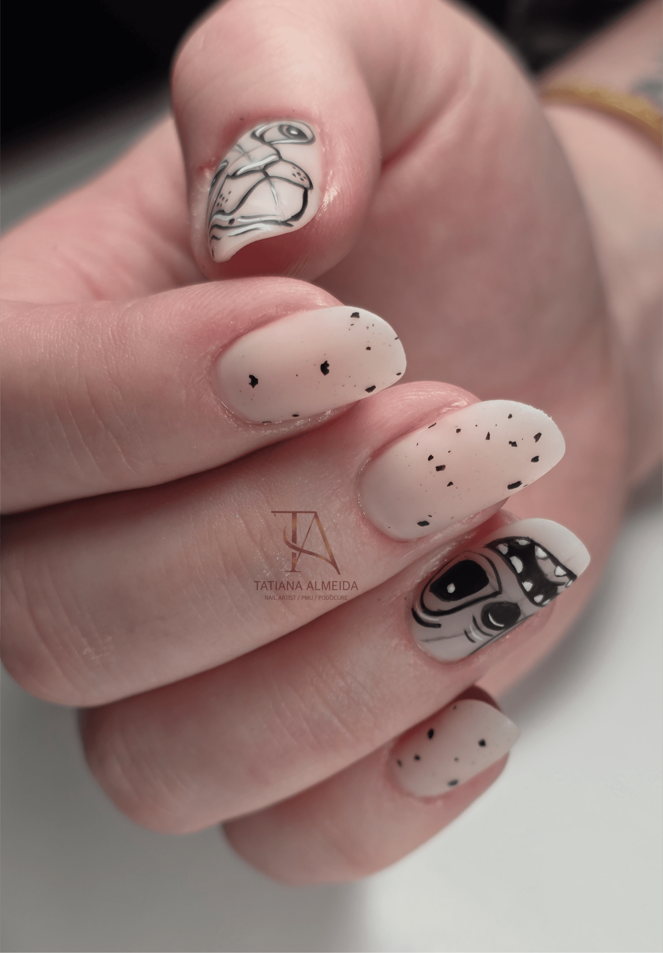 Manucure nude avec effet moucheté noir et illustrations artistiques du personnage Stitch.