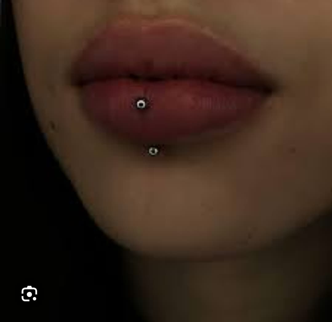 Gros plan de lèvres pulpeuses avec un piercing labret vertical et deux petites billes métalliques.