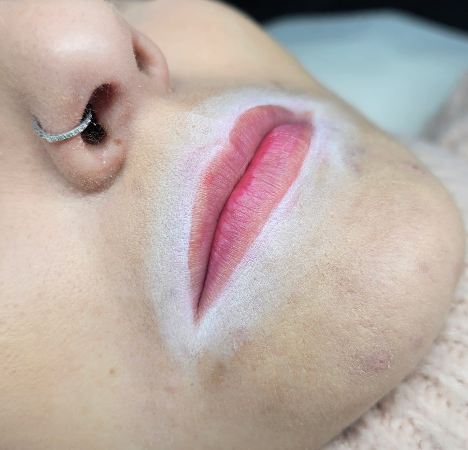 Lèvres roses tracées en blanc pour maquillage permanent et un piercing au septum argenté.